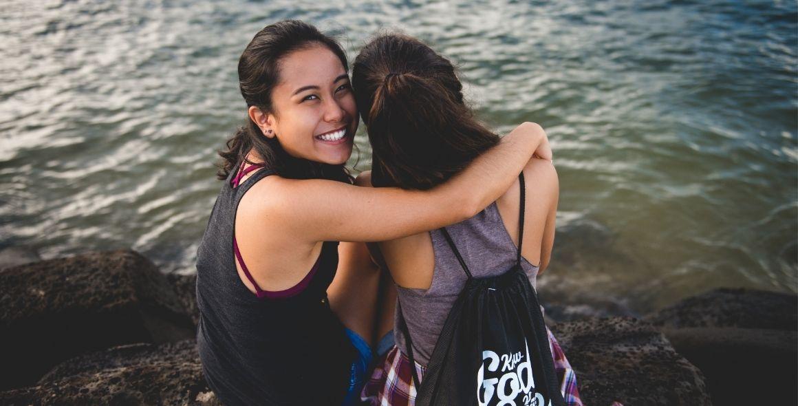 Two girls huggins by the water smiling